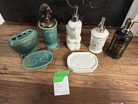Wide view of all bathroom items showing 7 pieces including toothbrush holder, soap dishes, containers, and soap dispensers in green ceramic, white ceramic, and dark brown colors