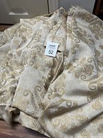 Curtains folded on the floor showing gold and beige paisley pattern, with MaxSold tag number 52 visible.