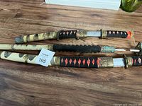 Three decorative Japanese style swords laid out on wooden floor, showing different sheath designs and handle wraps.