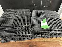 Stack of black rubber floor tiles with interlocking edges on wooden floor against black wall.