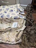 Photo showing the two sets of folded curtains with different fabric patterns, along with brown and beige twisted cord tiebacks with braided tassels.