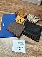 Six wallets and coin purses displayed on wooden floor, showing condition and designs.