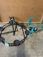 Photo showing black metal outdoor candle chandelier frame lying on the floor showing five candle holders and blue metal plant pot stand.