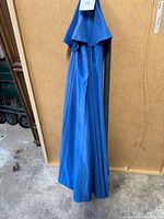 Closed blue fabric canopy of outdoor patio umbrella leaning against a board with label 22.