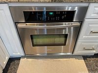 Front view of stainless steel digital wall oven installed in white cabinetry, control panel active with display reading 7:00
