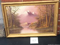 Framed oil on board painting showing a purple and mauve toned mountain and lake scene with trees and distant peaks.
