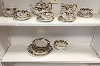 Full tea and serving ware set arranged on shelves showing cups, saucers, plates, teapot, creamer, and sugar bowl with matching floral and gold gilt design.