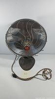 Front view of vintage KM space heater showing protective metal grill, logo badge, and cloth-covered electrical cord.