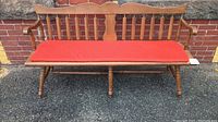 Front view of the spindle back maple wood bench with orange cushioned seat in outdoor setting.
