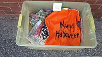 Plastic bin containing multiple folded throw pillowcases including an orange Halloween-themed pillowcase with 'Happy Halloween' text.