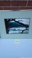 Framed coastal landscape painting with silhouetted tree branches, mountains, and ocean waves in muted blue and gray tones, signed by Teo Cooper.