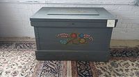 Front view of wooden chest showing hand-painted floral artwork and nailhead trim on lid edges.