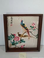 Framed embroidered artwork of two birds on a branch with flowers on a silk background.