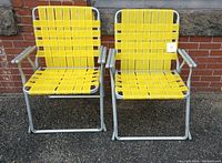 Front view of two vintage yellow aluminum folding lawn chairs with woven webbed seats and backs placed side by side.