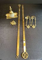 Photo showing entire assortment of brass items on dark fabric background, including wall hangers, curtain tie-backs, wall hook, and crumb catcher with brush.