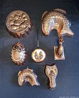 Top-down view of seven assorted copper items including jelly molds and decorative pieces arranged on black cloth.