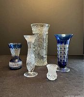 Front view of five assorted crystal and colored glass vases showing details of cut patterns and colors