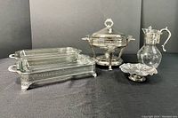 Photo showing all five assorted serving pieces including two rectangular silver-tone chafing dishes with glass inserts, a silver-tone chafing dish with lid, a silver-tone pedestal candy dish, and a glass water jug with silver-tone handle and lid.