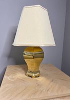 Full view front angle of brass lamp with white fabric shade on wooden table against grey wall.