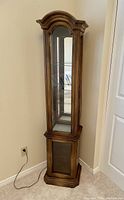 Front view of the wood curio cabinet showing the top glass door, mirrored back, and interior glass shelves with light cord visible.