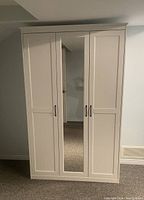 Front closed view of the white IKEA wardrobe with a mirror on the center door and two paneled doors on sides.