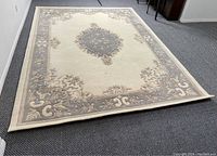Full view of the wool area carpet showing central medallion and floral border design, laid on a gray carpeted floor.