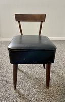 Front view of the walnut sewing chair showing the black vinyl cushioned seat and vertical backrest with tapered legs.