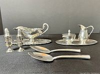 All sterling silver pieces arranged including salad servers, salt & pepper shakers, gravy boat with tray, ladle, cream jug, sugar bowl, and engraved tray.