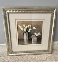 Full view of framed square print showing white tulips in silver-tone containers against muted background, frame shows wear.