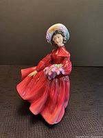 Front angle showing the figurine in a flowing red dress holding lilac flowers.