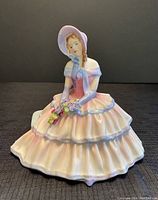 Front view of the Royal Doulton Daydreams figurine showing the seated young woman holding flowers, highlighting colors and detailing on the dress and bonnet.