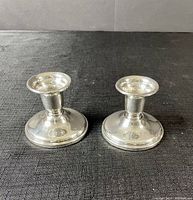 Pair of Birks sterling silver weighted candle sticks shown from front on black textured surface.