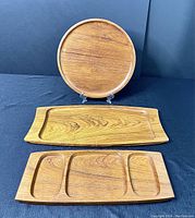 Full view of three teak serving trays including round tray, oblong tray, and compartmentalized tray
