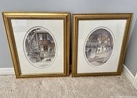 Pair of framed Trisha Romance color prints showing winter scenes, two gold-tone decorative frames with white matting and glass, standing against wall