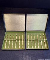 Two open boxes showing six gold-coloured bamboo-style seafood forks each, total 12 forks, inside original box with gold and green lining