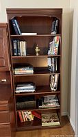 Front view of Palliser wood bookcase holding various books and a decorative brass urn, showing six shelves and details of the wood finish.