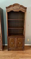 Front view of the Drexel Heritage wood veneer bookcase showing three open shelves and ornate two-door cabinet with brass ring pulls below.
