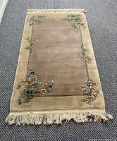 Full view of the rug laid out on a dark carpeted floor showing the overall design, color, and condition including the fringe at one end.