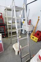 Full view of the 12 ft aluminum industrial ladder standing in a garage near shelves and tools. A small plastic step stool is positioned under the ladder.