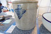 Front view of the crock showing the blue painted geometric design marked with the number '2'. Positioned on a table with a kitchen setting in the background.