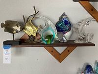 Five aquatic decor sculptures on a shelf including fish and dolphin shapes made from metal and glass.