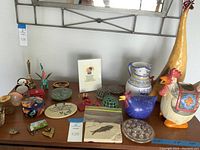 Photo of assorted decorative items including ceramic roosters, vintage flower frogs, sangria pitcher, fossil and other small decor pieces on a wooden surface
