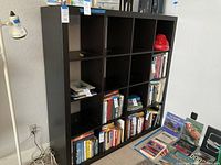 Front view of the black cube bookcase filled with various books in some cubes, showing the 16 equal square compartments in a 4x4 layout.