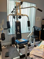 Front view showing BMI 9850 multi-exercise home gym machine with padded seats and arm press pads, weight stack visible behind.