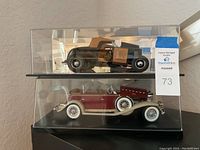 Two model cars in separate plastic display cases. Top is black 1932 Ford Roadster Deuce and bottom is dark red 1932 Cadillac V-16 Special Phaeton.