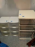 Two white plastic storage bins each with three translucent drawers alongside a metal wire rack storage unit with three wire mesh drawers and a solid top.