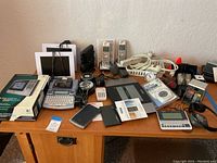 Wide view of table with various electronics including phones, label maker, dictionary, and remote control