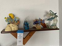Full view of five fish decor figurines on wooden shelf, showing all items in the lot clearly.