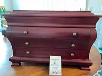 Front view of wooden jewelry box showing three drawers with round knobs and curved sides.