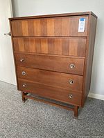 Front view of the teak chest of drawers showing drawer fronts and metal ring pull handles.